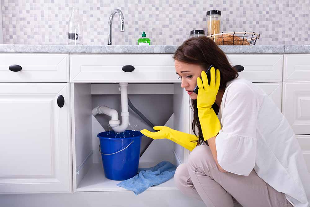 woman holding bucket under leaking sink pipe while calling plumber